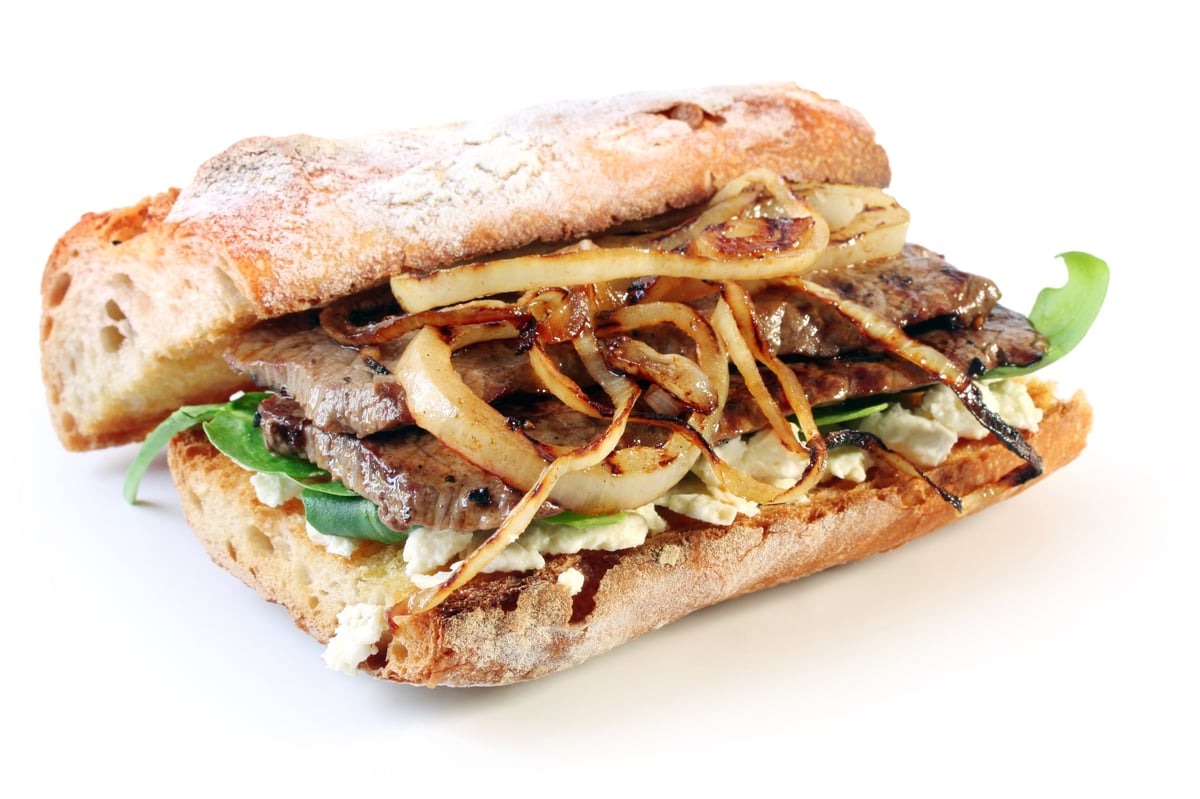 Steak sandwich with beef on toasted bread, goat cheese, spinach and grilled onion
