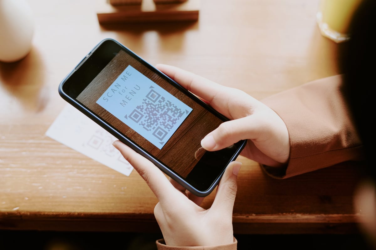 Persona escaneando código QR para acceder al menú digital en restaurante con bebida y mesa de madera