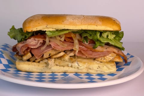 Gourmet sandwich on toasted roll with bacon, lettuce, and crispy shoestring fries served on blue checkered paper