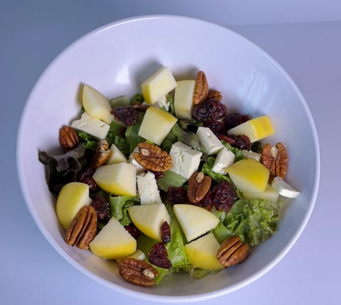 Salad bowl with mixed greens, diced apples, crumbled cheese, dried cranberries, and toasted pecans