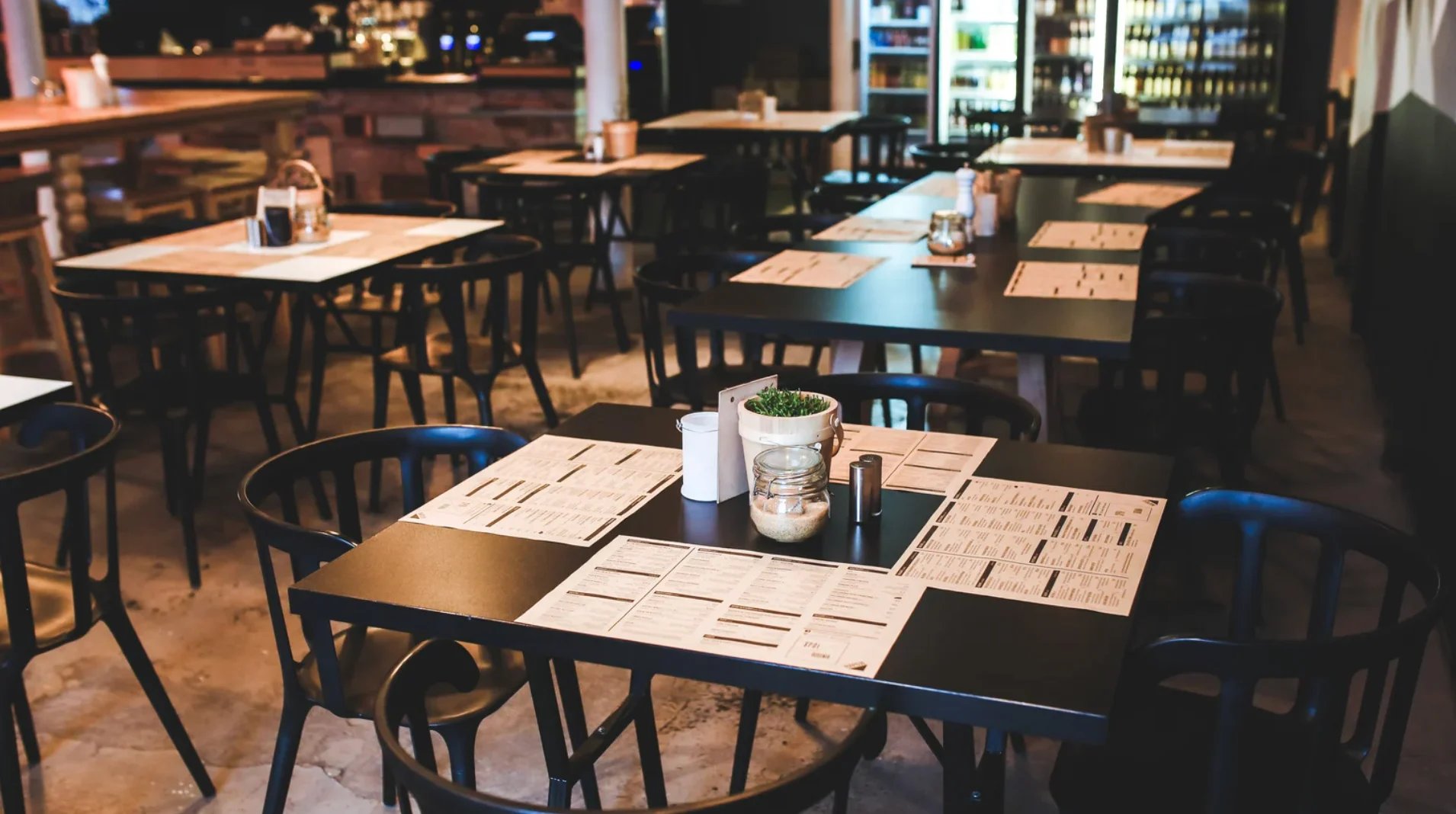 Restaurant interior with wooden tables, black chairs, menus, and glasses in warm lighting