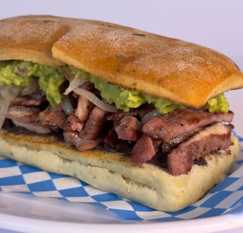 Roast beef sandwich on seeded roll with lettuce and onions, served on blue checkered paper