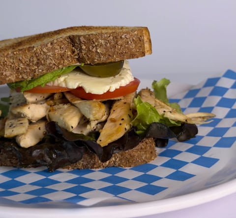 Gourmet sandwich with whole wheat bread, sautéed mushrooms, melted cheese, tomato, and greens on checkered paper