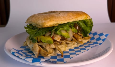 Gourmet sandwich with pulled meat, fresh lettuce, and crispy fries on a blue and white checkered paper-lined plate