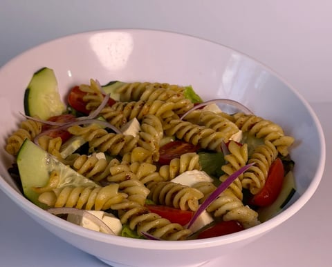 Bowl of tri-color rotini pasta salad with cucumbers, tomatoes, onions, and cheese cubes